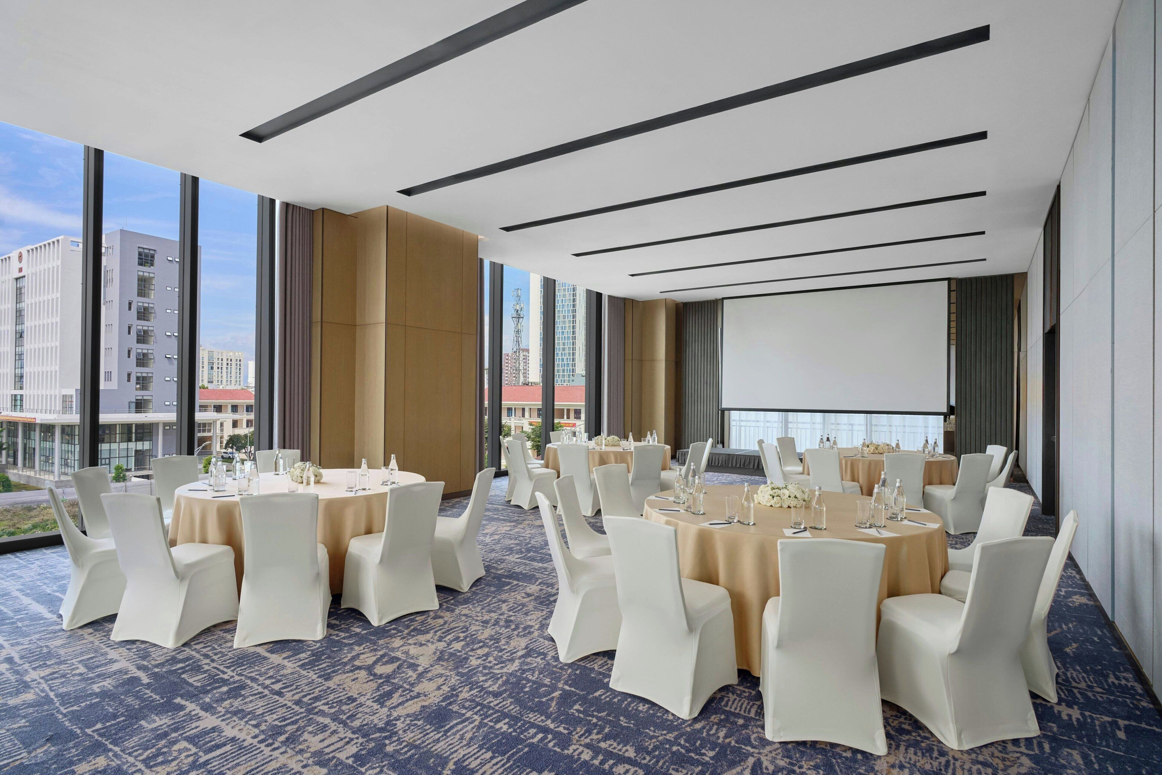 A conference room with round tables, white chairs, and a large screen.
