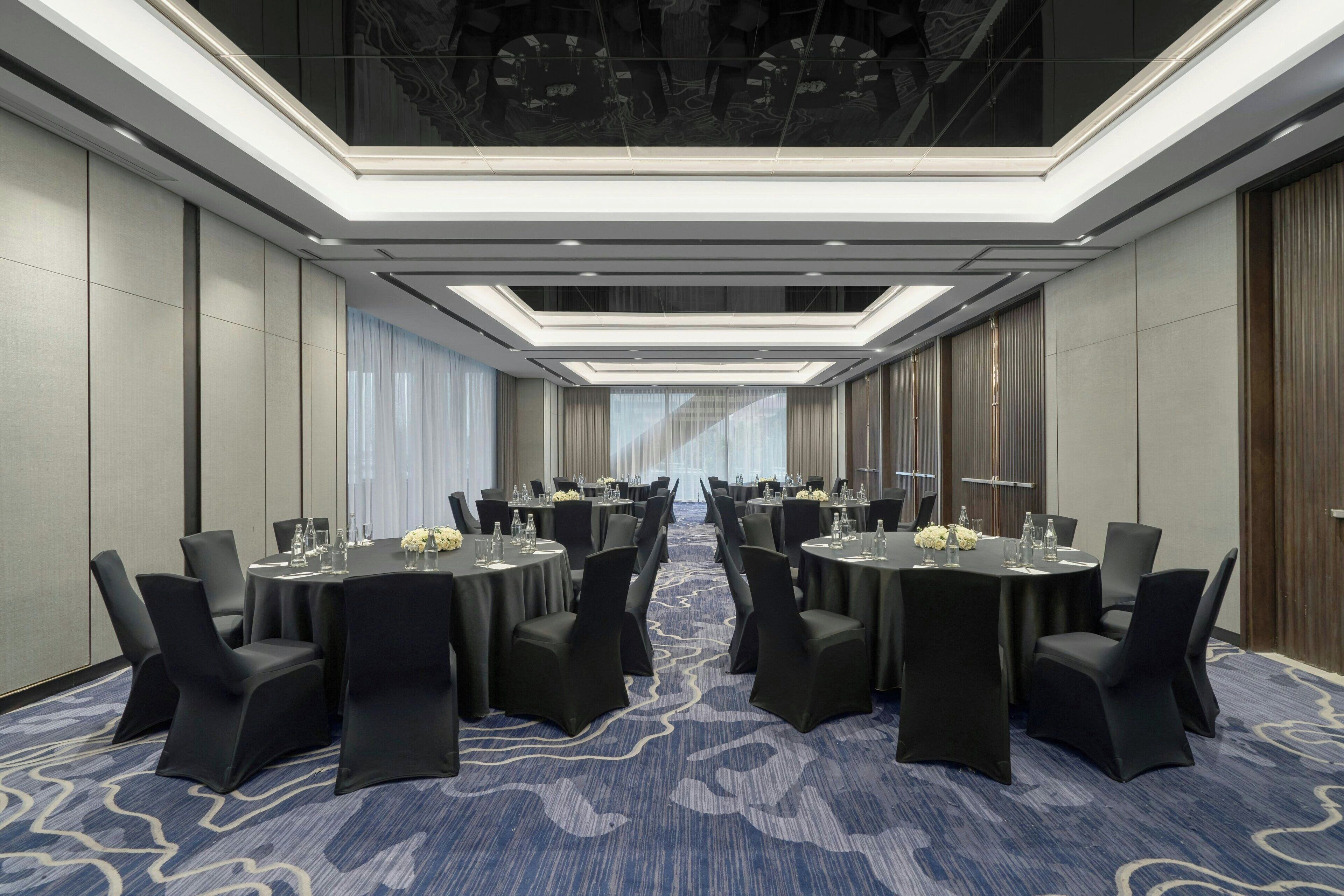 A conference room with multiple tables and chairs, equipped with water glasses and floral centerpieces.