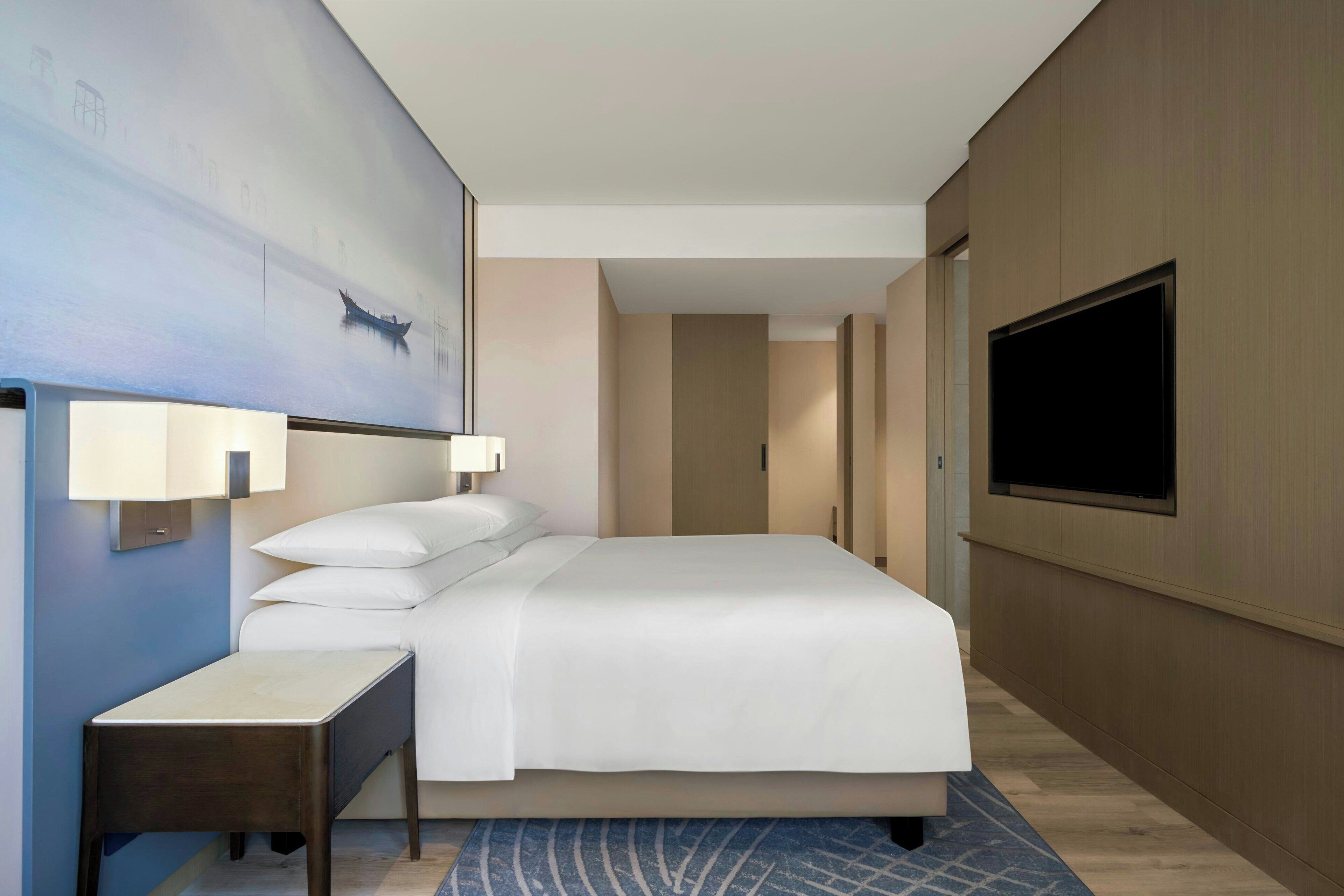 A hotel room with a large bed, bedside tables, a flat-screen TV, and a painting on the wall.