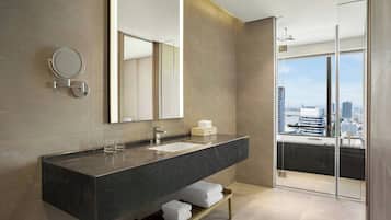 Une salle de bain moderne avec un grand miroir, un plan de toilette en marbre foncé, une douche à parois de verre et une vue sur la ville.