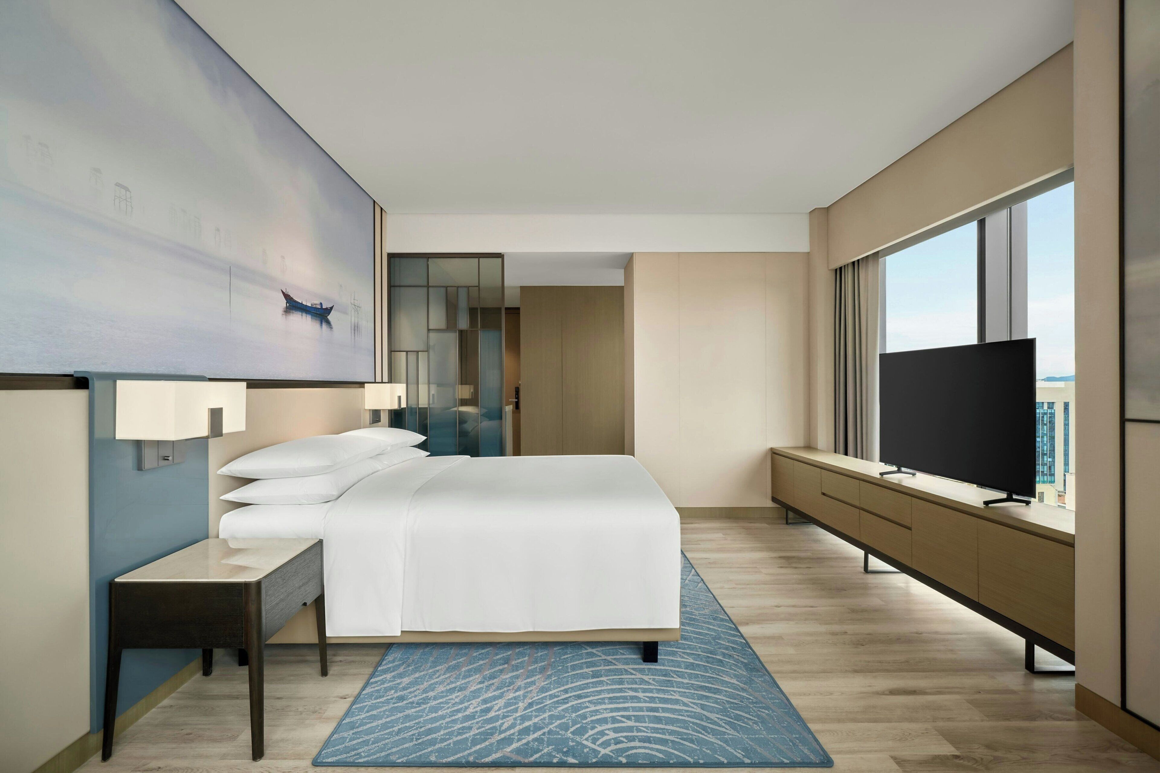 Habitación de hotel moderna con una cama grande, televisión, escritorio y vistas a la ciudad.