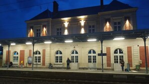 Ein Bahnsteig mit einem Bahnhof im Hintergrund, auf dem 