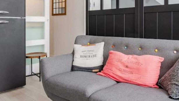 Ein modernes Wohnzimmer mit einem grauen Sofa, einer schwarzen Kommode und einer außergewöhnlichen Leuchte.