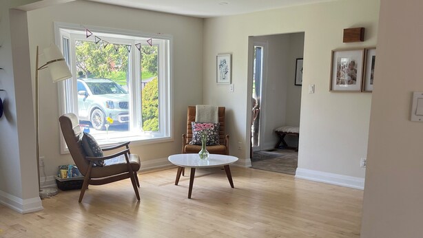 A spacious living room with hardwood floors, a large window with a view of a parked car, a chair, a small table, and a potted plant. - Darling Bungalow in the heart of quaint Inglewood, On. 15 minutes from Osprey! (Inglewood)