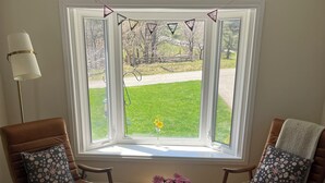 A room with two brown leather chairs with floral cushions, a white round table, and a window with a view of a green lawn and trees. - Darling Bungalow in the heart of quaint Inglewood, On. 15 minutes from Osprey! (Inglewood)