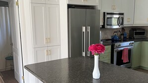 A kitchen with white cabinets, a stainless steel refrigerator, a microwave, and a stove. There is a vase with flowers on the counter. - Darling Bungalow in the heart of quaint Inglewood, On. 15 minutes from Osprey! (Inglewood)