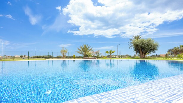 A clear blue swimming pool with a tiled edge, surrounded by greenery and a clear sky. - Palm & Sea apartment (Los Alcazares)