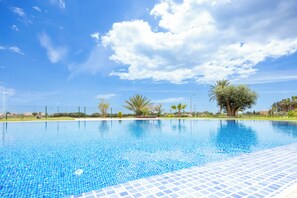 Una piscina azul cristalina con borde de azulejos, rodeada de follaje y un cielo despejado.