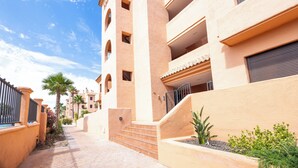 A multi-story hotel with a central courtyard, featuring a staircase leading to the upper floors, surrounded by palm trees and a clear blue sky. - Palm & Sea apartment (Los Alcazares)