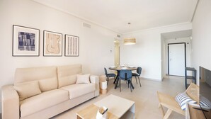 A modern living room with a beige sofa, a wooden coffee table, and a dining area with a round table and chairs. - Palm & Sea apartment (Los Alcazares)