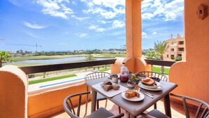 A balcony with a table set for breakfast, overlooking a golf course and buildings. - Palm & Sea apartment (Los Alcazares)