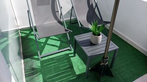 A balcony with a green artificial turf floor, two grey mesh chairs, a small table with a potted plant, and a metal pole. - Fortezza Nest - Old Town Rethymno (Rethymno)