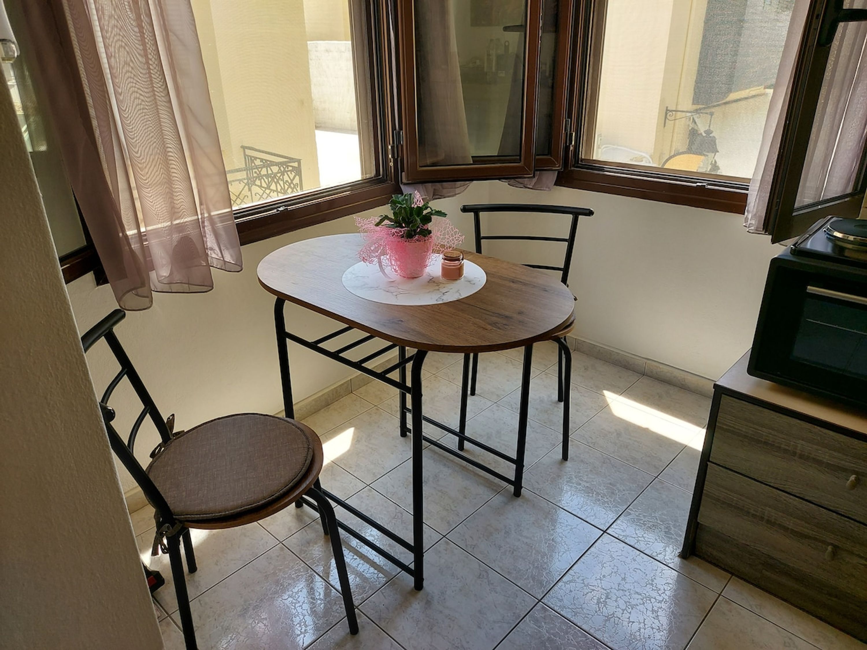 A small dining area with a round table, two chairs, a potted plant, and a cabinet.