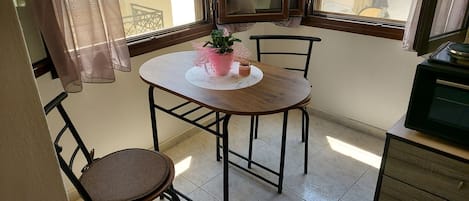 Un pequeño comedor con una mesa redonda, dos sillas, una planta en maceta y un aparador.