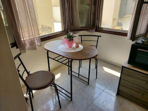 Un pequeño comedor con una mesa redonda, dos sillas, una planta en maceta y un aparador.