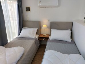 A hotel room with two single beds, a bedside table with a lamp, a power outlet, and a window with curtains. - Fortezza Nest - Old Town Rethymno (Rethymno)