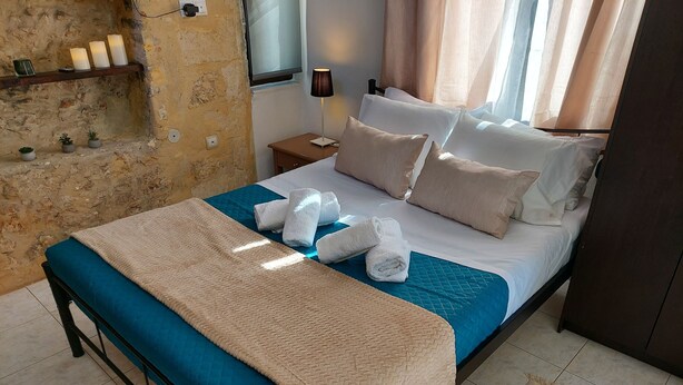 A neatly made bed with a blue and beige bedspread, white pillows, and rolled towels. - Fortezza Nest - Old Town Rethymno (Rethymno)