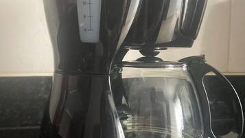 Una cafetera negra con un depósito de agua transparente y una balanza graduada con medidas.