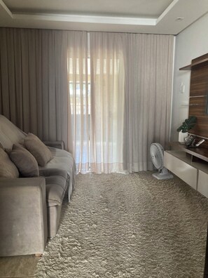 Una sala de estar con sofá, cortinas, ventilador y planta.