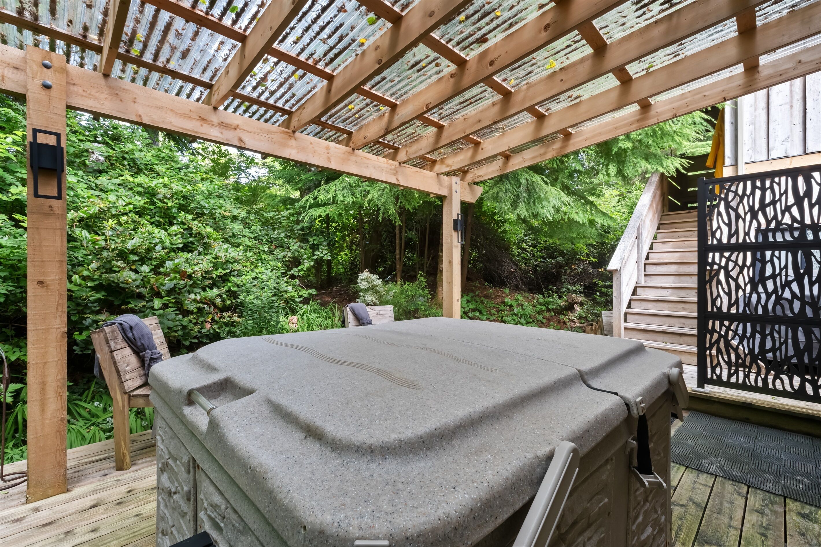 A hot tub under a wooden pergola with a view of a forested area.