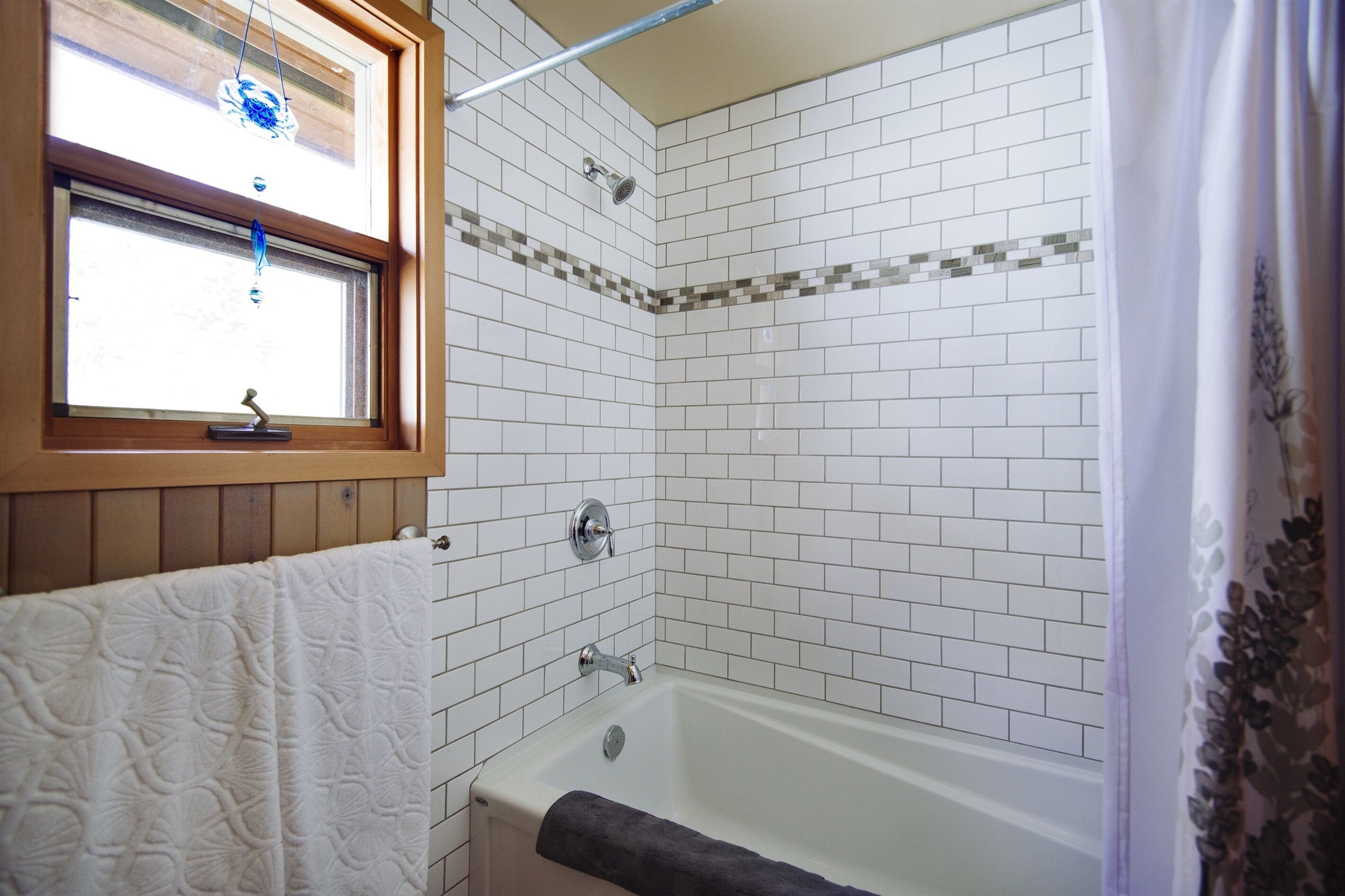 Ein Badezimmer mit Badewanne, einem Fenster mit aufgehängtem Handtuch und einer Duschkabine.