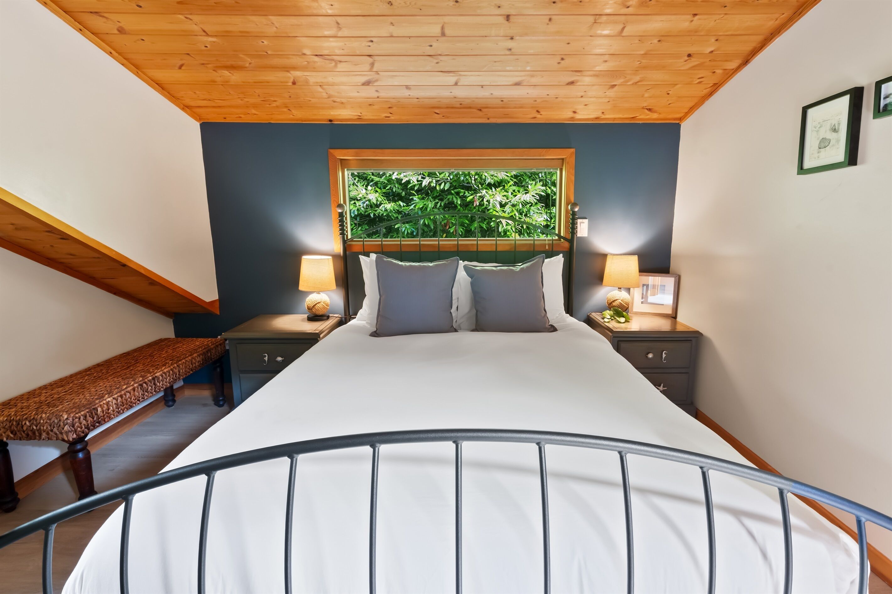 Ein Schlafzimmer mit einem Bett, Holzboden, zwei Nachttischen mit Lampen, einer Bank und einem Fenster mit Blick ins Grüne.