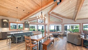 A spacious kitchen with a central island, wooden ceiling, large windows, and a dining area with a bench and chairs.