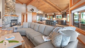 A modern living room with a stone fireplace, a large L-shaped gray sofa, and a dining area with a wooden table and chairs.