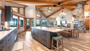 A spacious kitchen with a large island, wooden ceiling beams, and a stone fireplace.