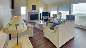 A living room with wicker furniture, a fireplace, and a television. - Whispering Sands Beachfront | Community Pool (Galveston)