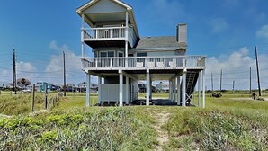 A two-story beachfront house with a balcony, a covered porch, and a small staircase leading to the upper level. - Whispering Sands Beachfront | Community Pool (Galveston)