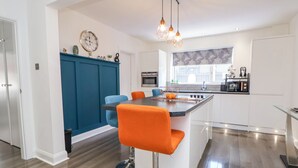 Una cocina moderna con una isla central, un muro azul decorativo y una zona de comedor con sillas naranjas.