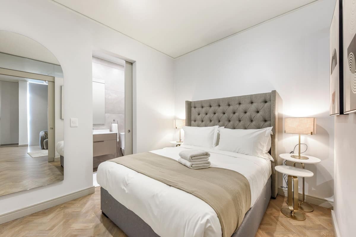 Ein modernes Hotelzimmer mit einem großen Bett, einem Nachttisch, einem Spiegel und Blick ins Bad.