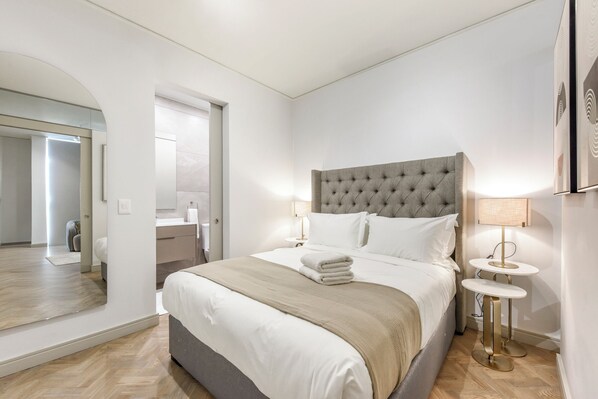 Une chambre d’hôtel moderne avec un grand lit, une table de chevet, un miroir et une vue sur la salle de bain.