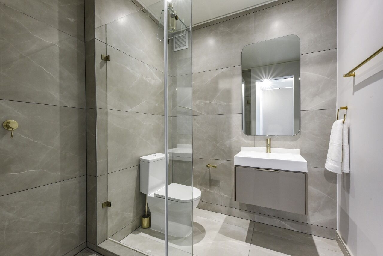 Un baño moderno con ducha envuelta en vidrio, inodoro y lavamanos con espejo.