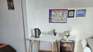 A small, tidy room with a wooden floor, a white table with a kettle, a small cabinet, and a chair. There are posters on the wall and a rug on the floor. - Apartment steps from Mall Arauco Maipú, Parking, wi fi. (Maipú)