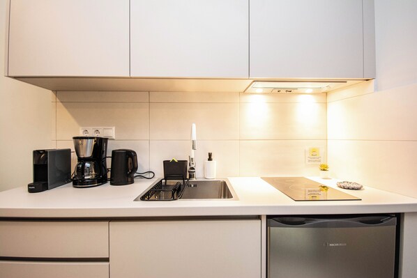 A modern kitchen with white cabinets, a built-in dishwasher, a coffee maker, and a sink. - Basil Central Studio - by Checkin (Heraklion)