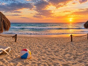 Una playa con una barrera de cuerda, una pelota de playa y un paraguas de paja.