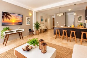 Una sala de estar moderna con un televisor grande, un comedor con taburetes de bar y una cocina con barra.