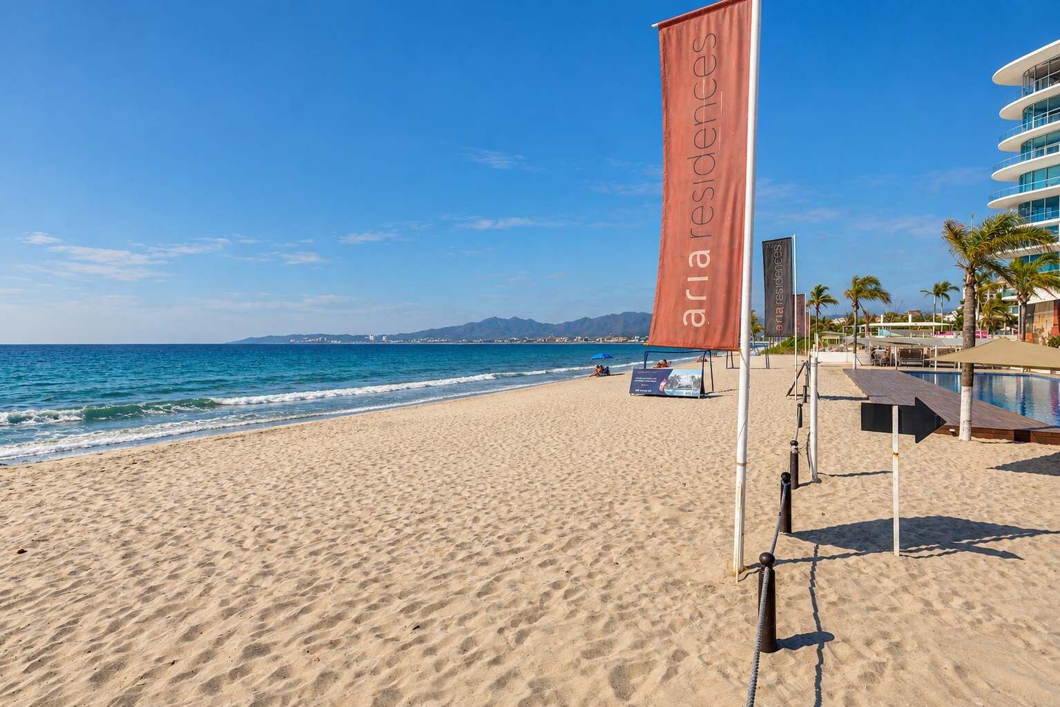 Ein Strand mit einer Flagge, einem Pool und einem Gebäude im Hintergrund.