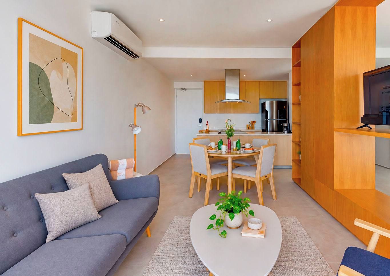 Un salon moderne avec un canapé gris, une table basse agrémentée d’une plante, et un coin repas avec des chaises en bois et une table dressée pour quatre personnes.