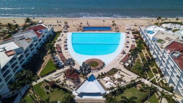 A resort with a large central pool, beachfront location, and multiple buildings with balconies.