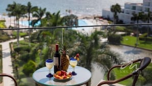 A balcony with a table set for two, overlooking a beach and pool area.