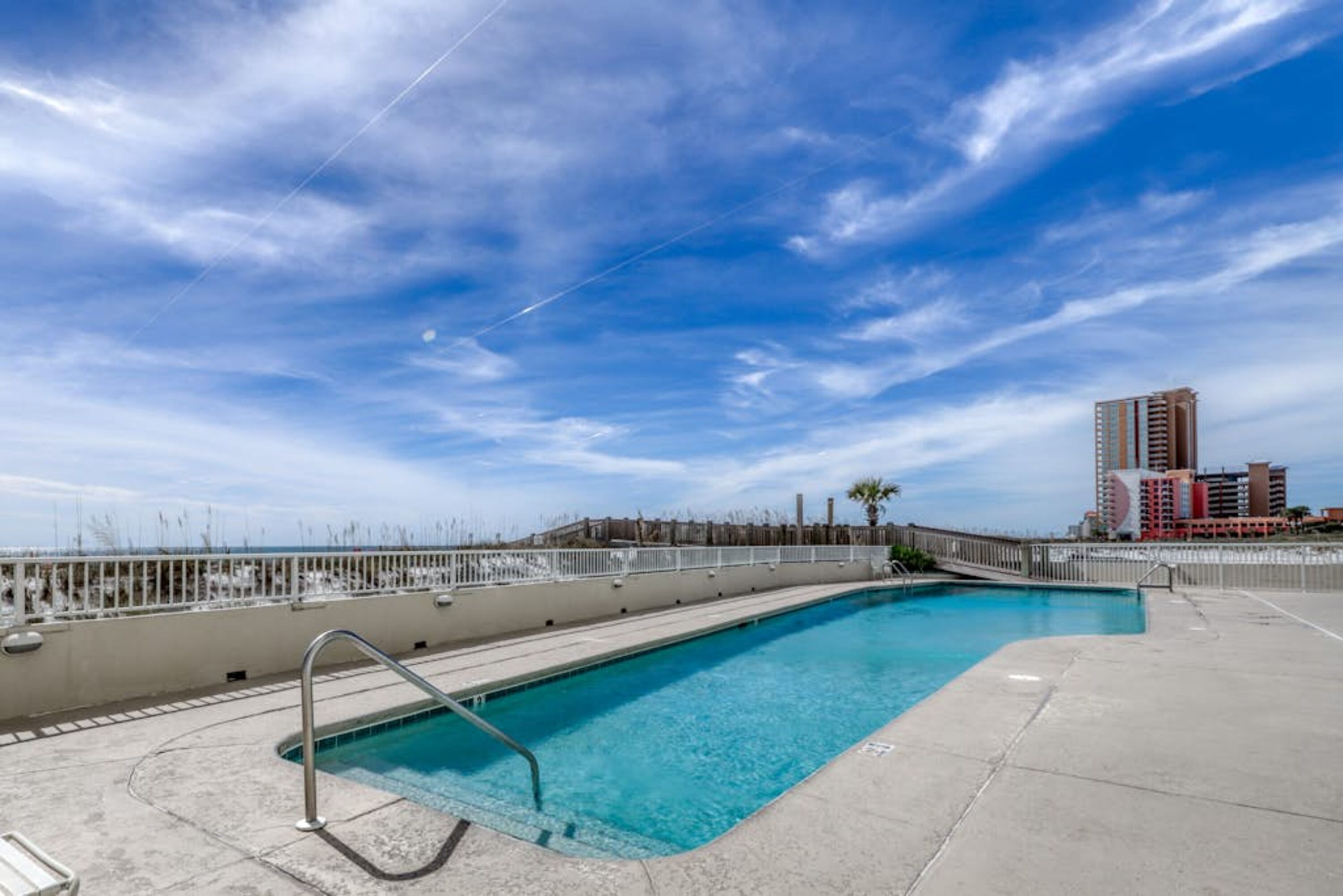 A swimming pool with a metal ladder, surrounded by a concrete deck and a white fence.