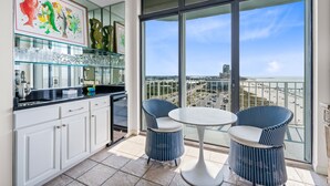 A balcony with a white table and two blue chairs, overlooking a beach and cityscape. - Summerchase Penthouse 1 (Orange Beach)