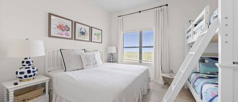 A bedroom with a bunk bed, a white bedspread, a nightstand with a lamp, and framed pictures on the wall.