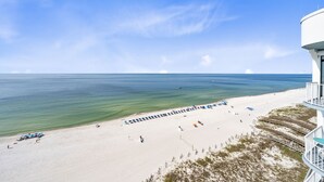 A beach with a white building, clear blue sky, and calm sea. - Summerchase Penthouse 1 (Orange Beach)