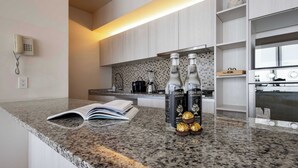 A modern kitchen with granite countertops, a built-in oven, and a backsplash of small tiles. There are two bottles of Casa del Agua on the counter, and an open book beside them.