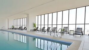An indoor swimming pool with clear water, surrounded by lounge chairs and large windows.