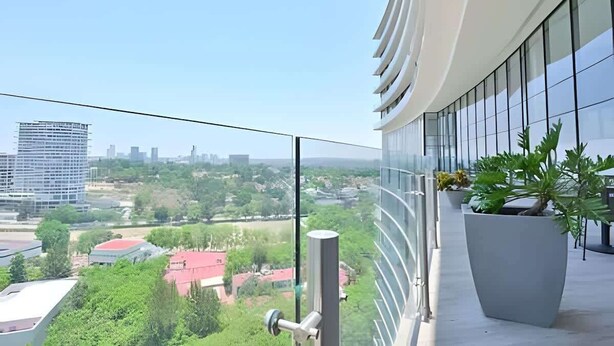 A balcony with a view of a cityscape, including buildings and greenery.